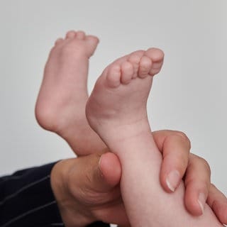 Eine Hebamme hebt die Füße eines wenige Wochen alten Babys, während sie es wickelt. (Symbolbild)