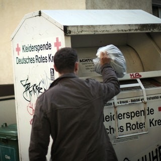 Ein Mann wirft einen Sack in einen Altkleidercontainer des DRK 