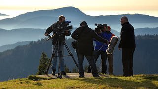 Ein SWR Team beim Dreh. Im Hintergrund ist ein in Nebel gehülltes Bergpanorama zu sehen.