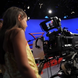 Ein Mädchen steht im Flutlicht-Fernsehstudio vor einer Kamera